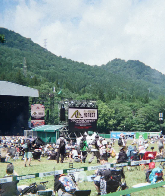 苗场的山脊与云层下,Fuji Rock 森林舞台前的草坡上散坐着观众。
